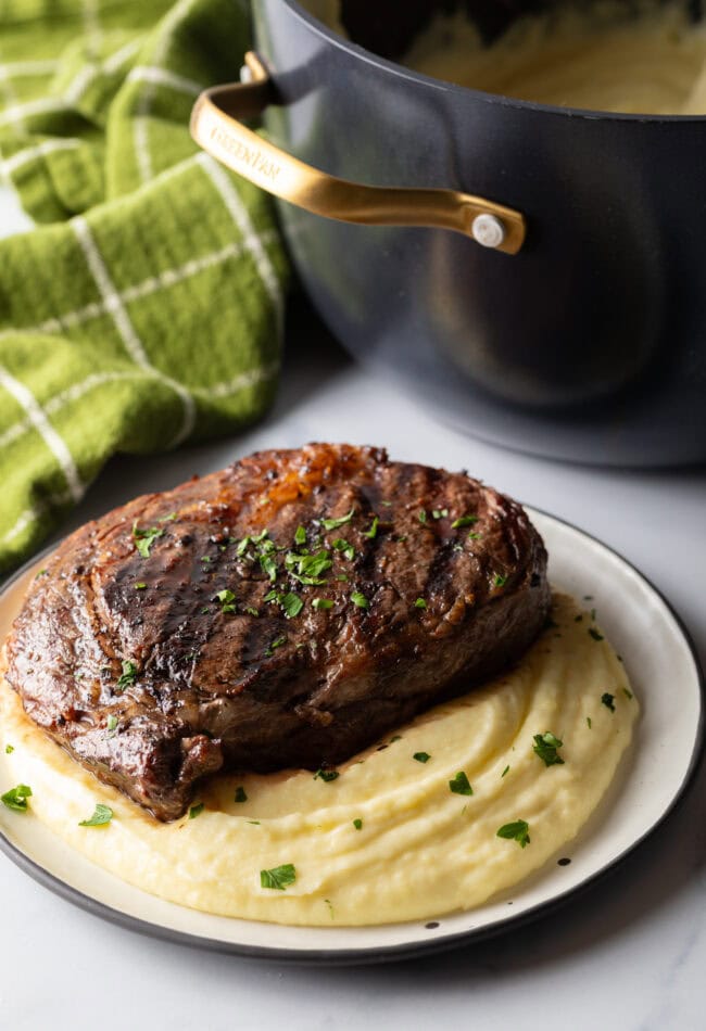 Grilled steak on top of a bed of whipped potatoes.