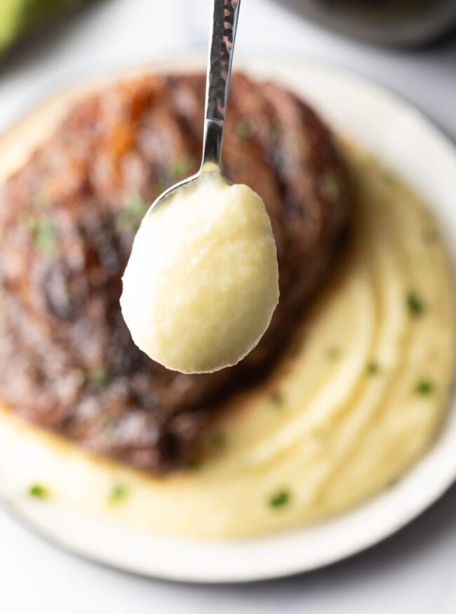 Grilled steak on top of a bed of whipped potatoes. A spoonful of potatoes is shown to camera.
