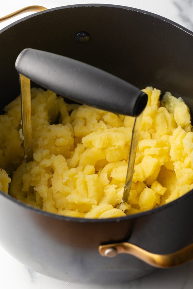 Using a hand masher to mashed cooked yellow potatoes.