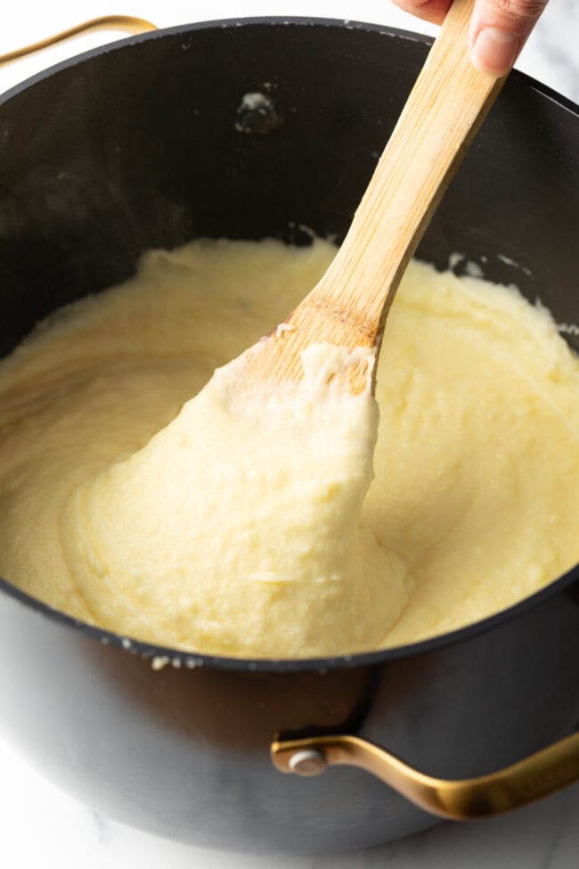 Creamy whipped potatoes in a black large pot, with a wooden spoon in the pot.