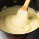 Creamy whipped potatoes in a black large pot, with a wooden spoon in the pot.