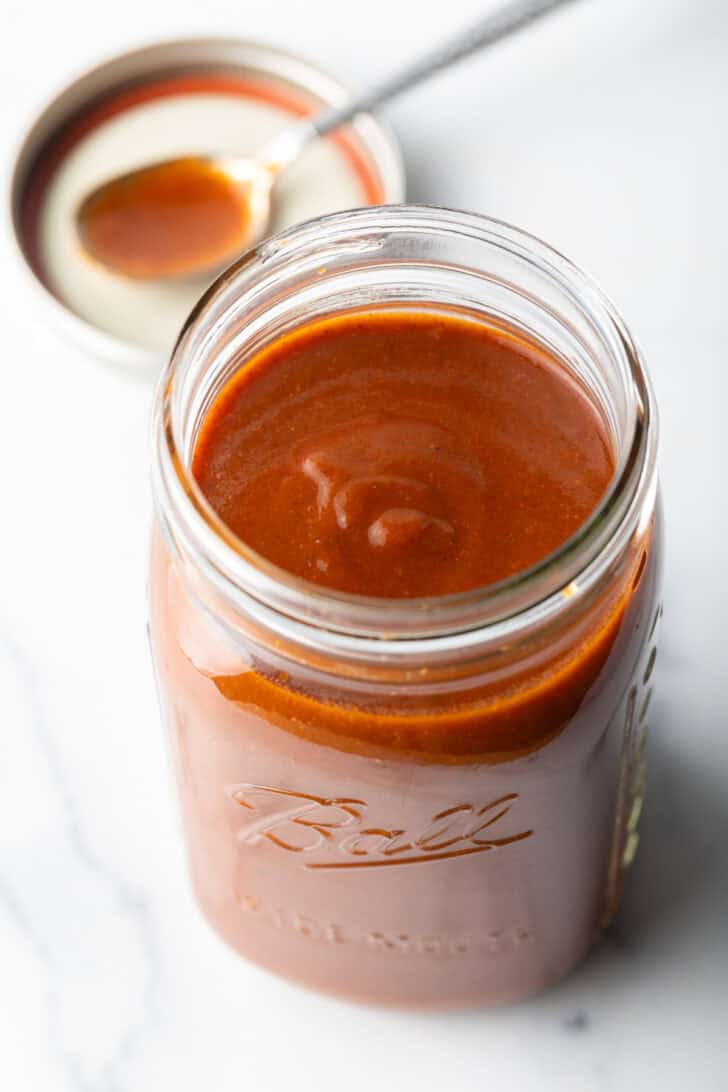 Top down view of red sauce in a large glass jar.