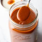 Spoonful of red enchilada sauce being held to camera over a large jar.