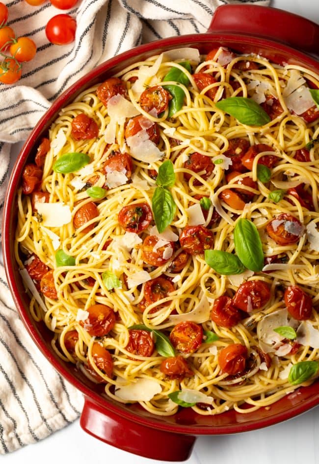 Spaghetti pasta with roasted tomatoes coating them in a large pot. 
