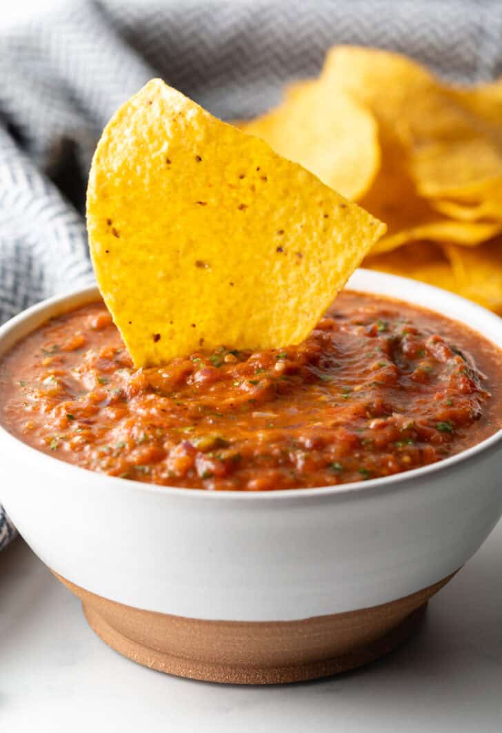 White bowl of roasted tomato salsa. A tortilla chip is sticking out of the salsa.