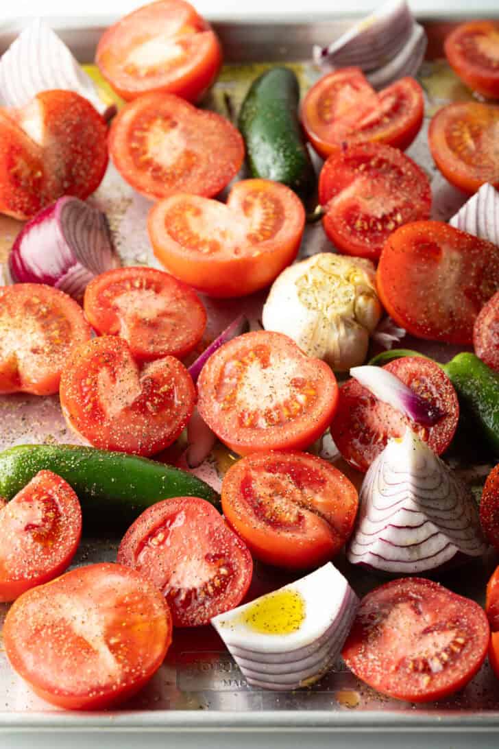 Top down view baking sheet brimming with fresh raw sliced tomatoes, jalapeno, and red onion chunks.