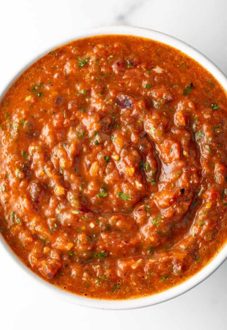Top down view of a white bowl of red roasted tomato salsa.