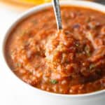 A metal spoon is showing a scoop of roasted salsa scooped from a white bowl.