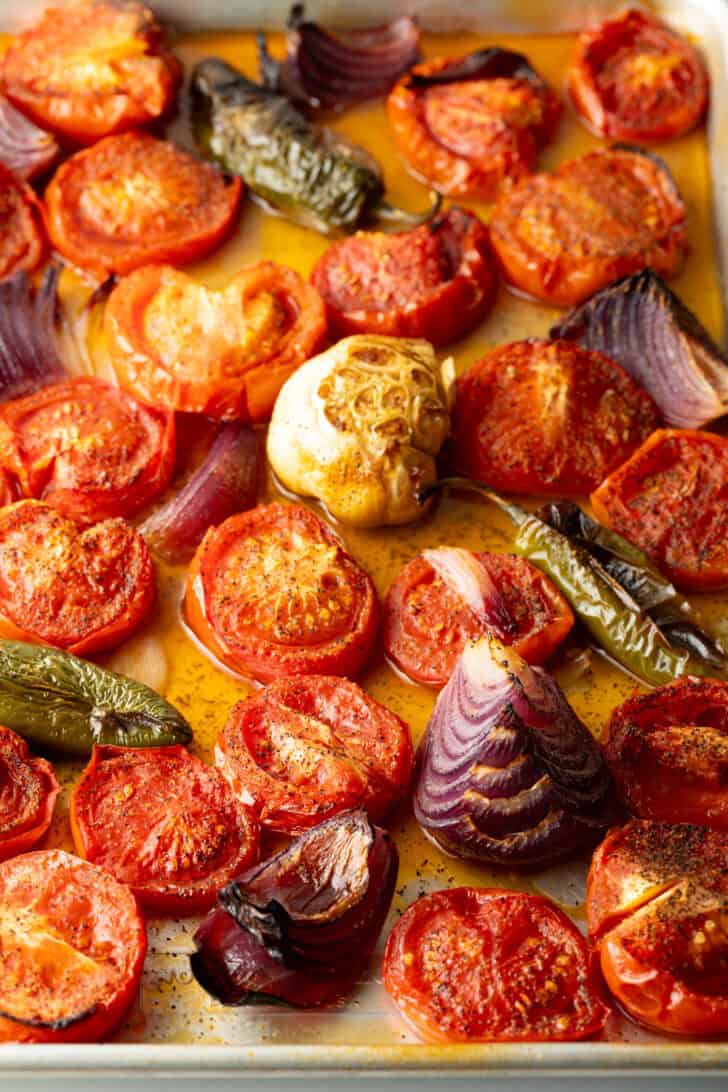 Top down view baking sheet brimming with roasted sliced tomatoes, jalapeno, and red onion chunks.