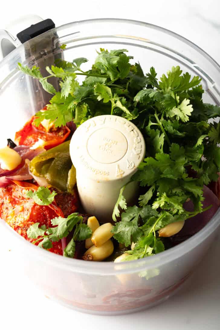 Food processor with fresh cilantro, tomatoes, jalapeno, and onion.