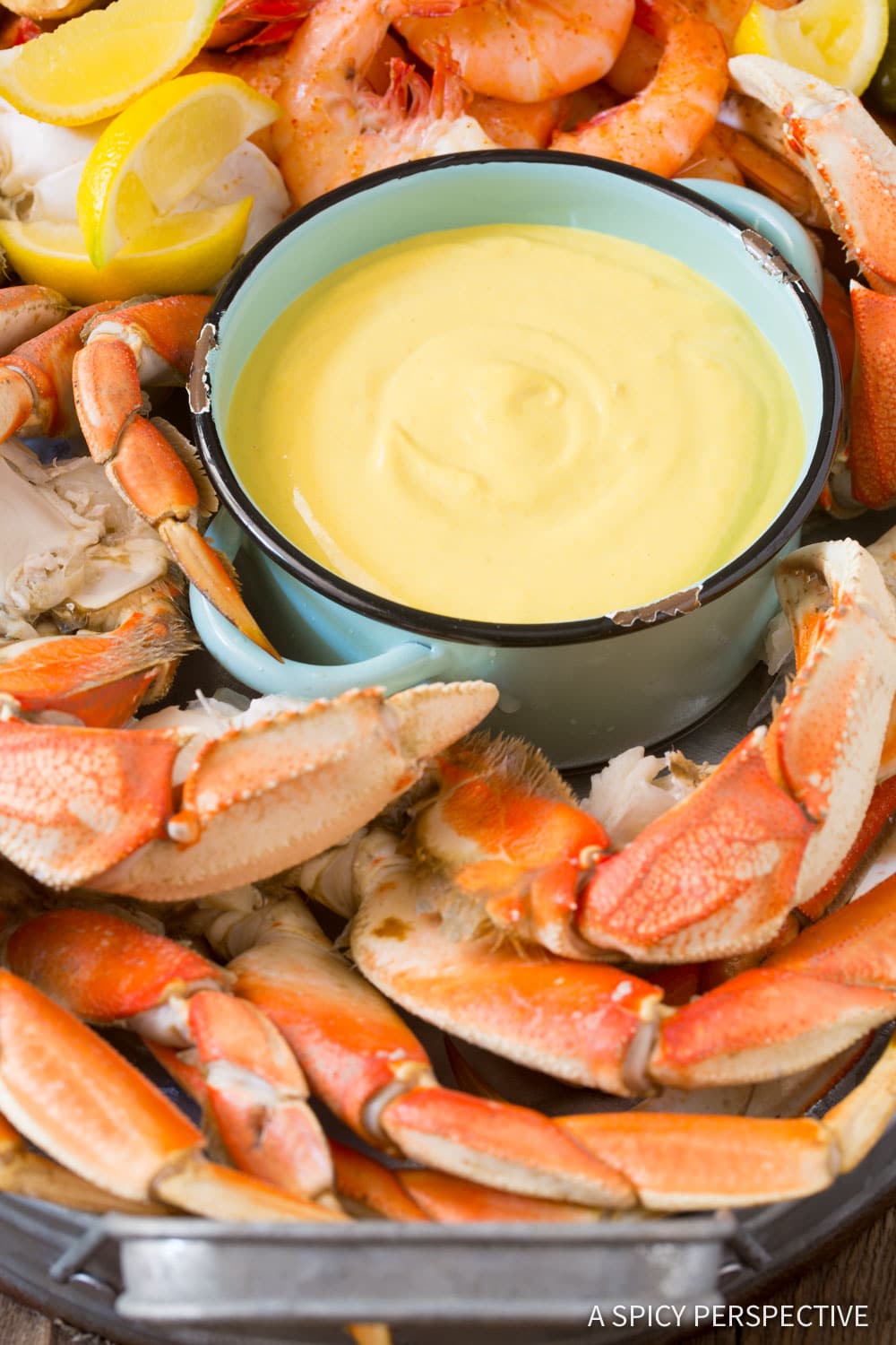 Shrimp, crab and lemon wedges on a platter next to a bowl of yellow seafood mustard sauce. 