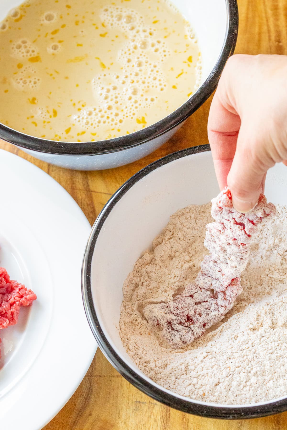 Hand holding the raw beef and dipping it in batter and flour to fry.