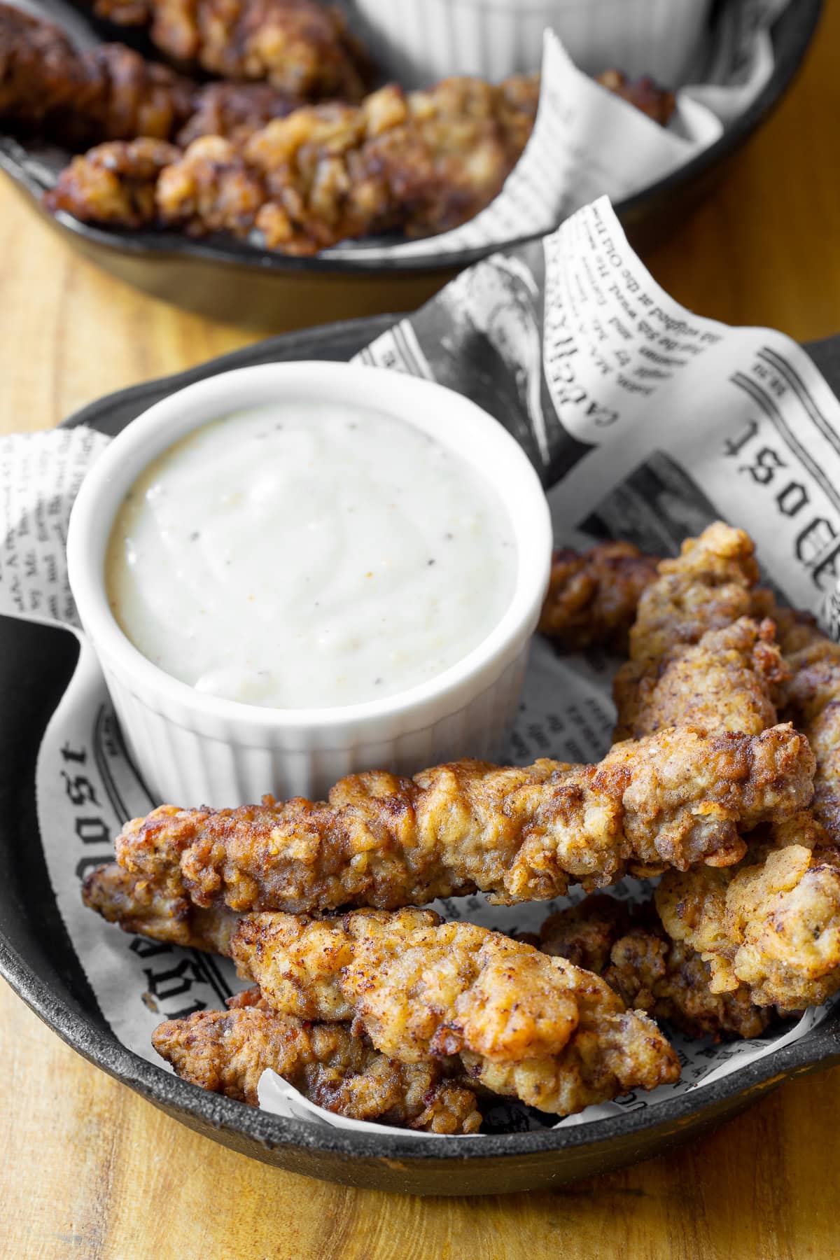 Steak Fingers with Country Gravy #ASpicyPerspective #SteakFingers #SteakFingersRecipe #HowtoMakeSteakFingers #CountryGravy #CountryGravyRecipe #HowtoMakeCountryGravy #Snack #PartySnack steak fingers recipe in a cast iron plate next to a saucer of gravy.