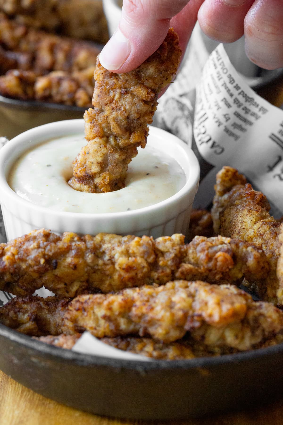 Hand dipping piece of chicken fried steak fingers into a small ramekin of gravy.