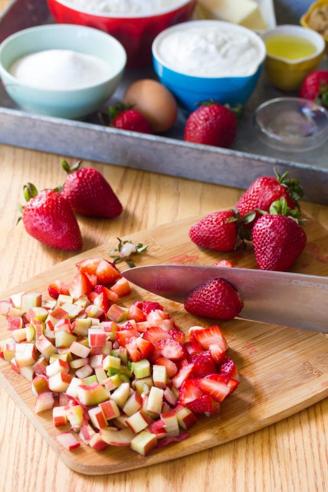 Chef's knife chopping rhubarb and strawberries on a wooden cutting board. 