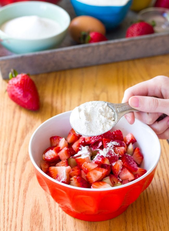 Hand sprinkling flour into a small bowl of strawberries. 