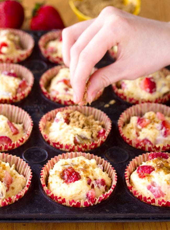 Hand sprinkling brown sugar on top of muffins before being baked. 