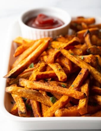 Piles of cooked sweet potatoes on a large serving pan with a white ramekin of ketchup.