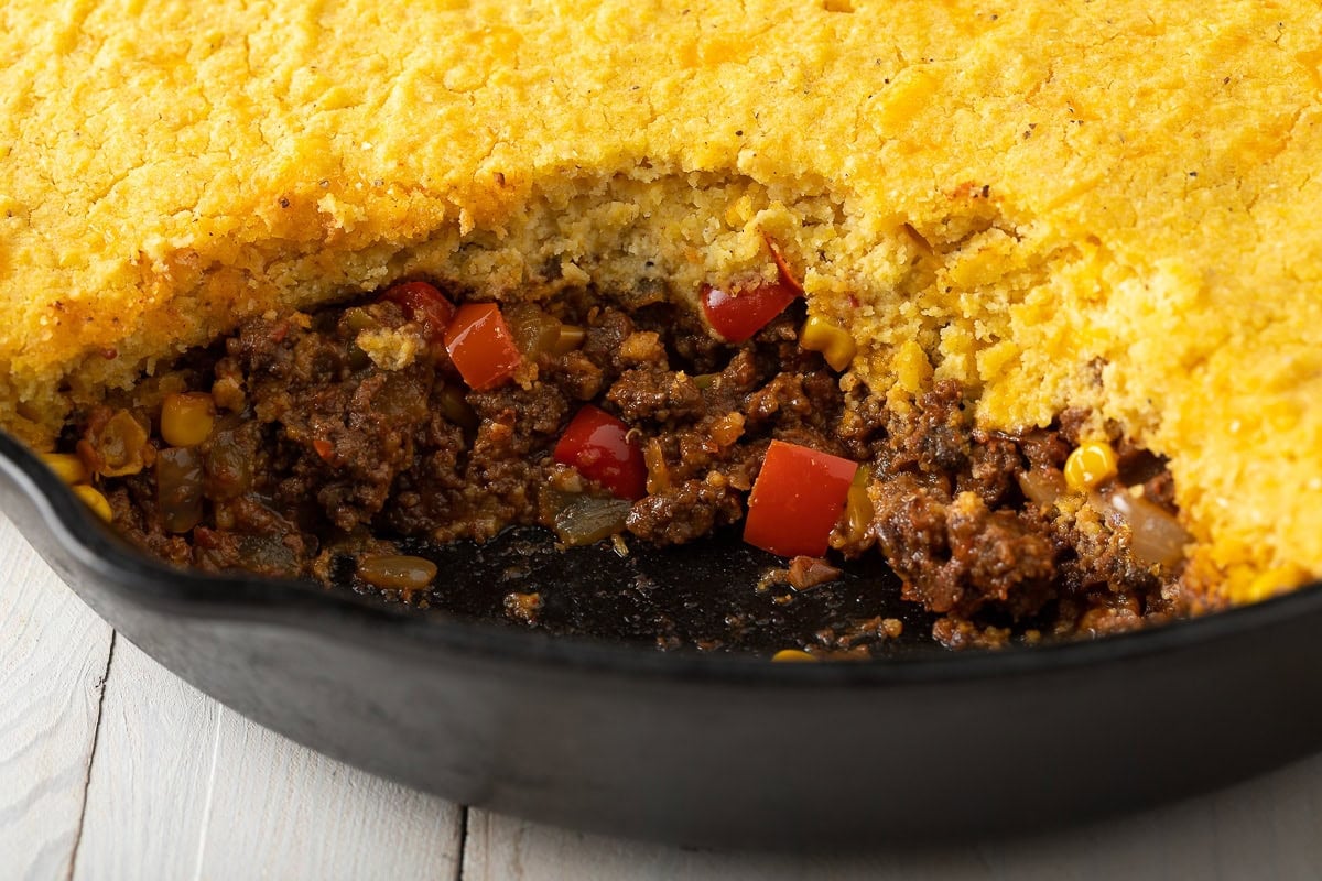 Tamale pie in a cast iron skillet with a portion missing. 