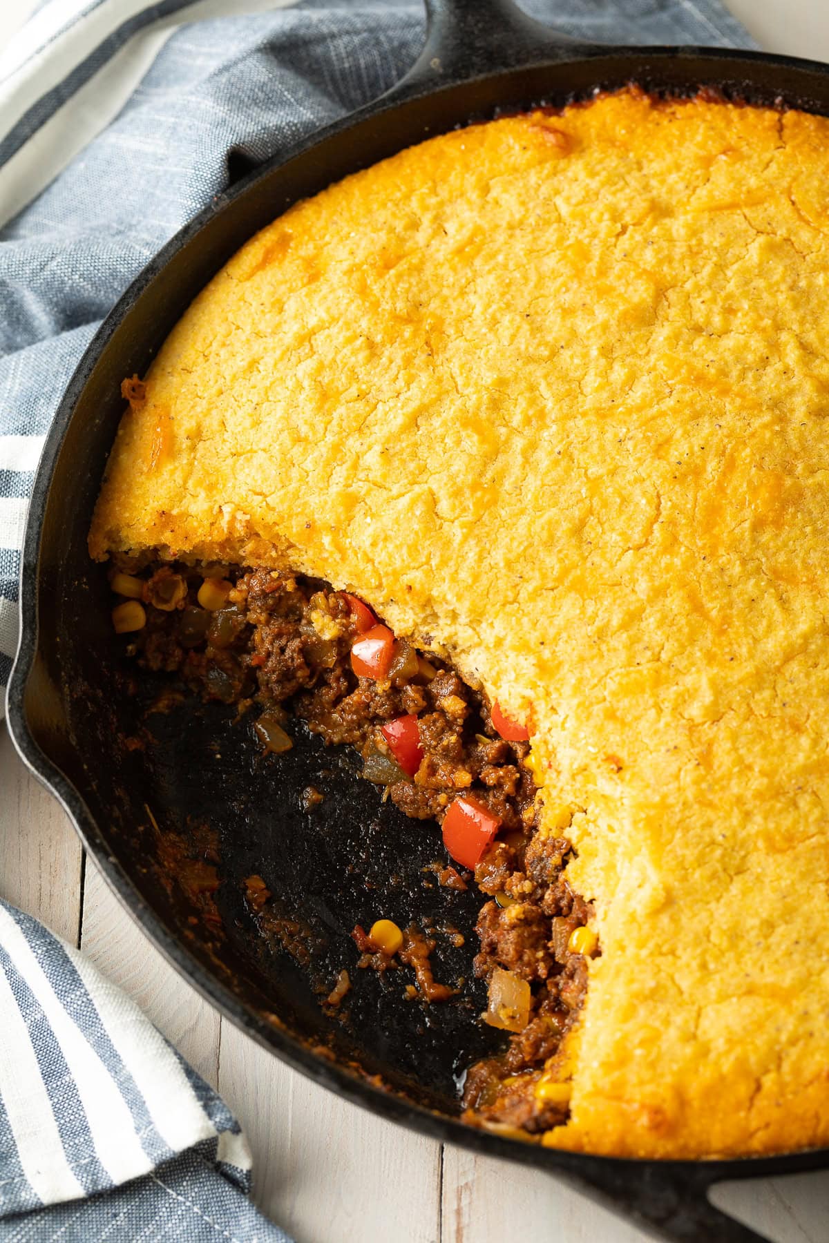 Overhead shot of tamale pie in a cast iron pan with a portion gone to show the layers. 
