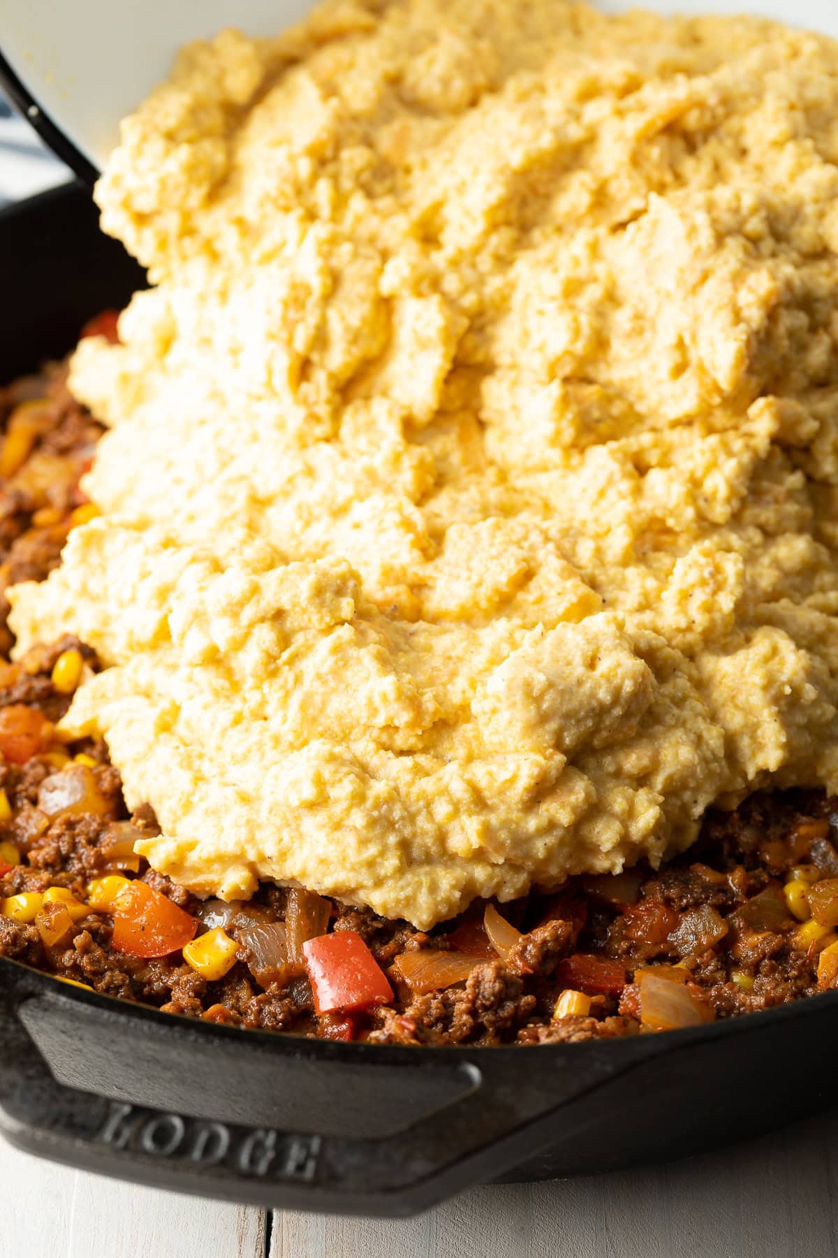 Corn masa topping being layered on top of the meat. 