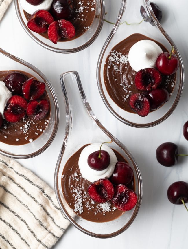 top view budino with chocolate individual servings, with pitted cherries and whipped cream with sea salt on each