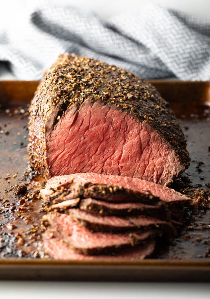 Cooked beef round roast on a metal baking pan. The front half of the roast has been thinly sliced.