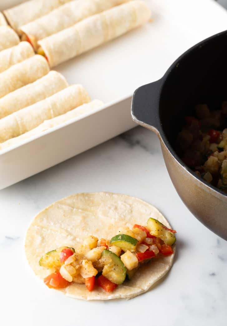 Corn tortilla filled with chopped cooked vegetables, ready to roll and place in a baking dish.