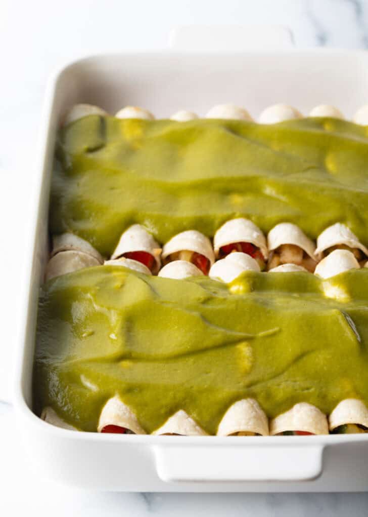 Two rows of enchiladas in a baking dish covered with green sauce.