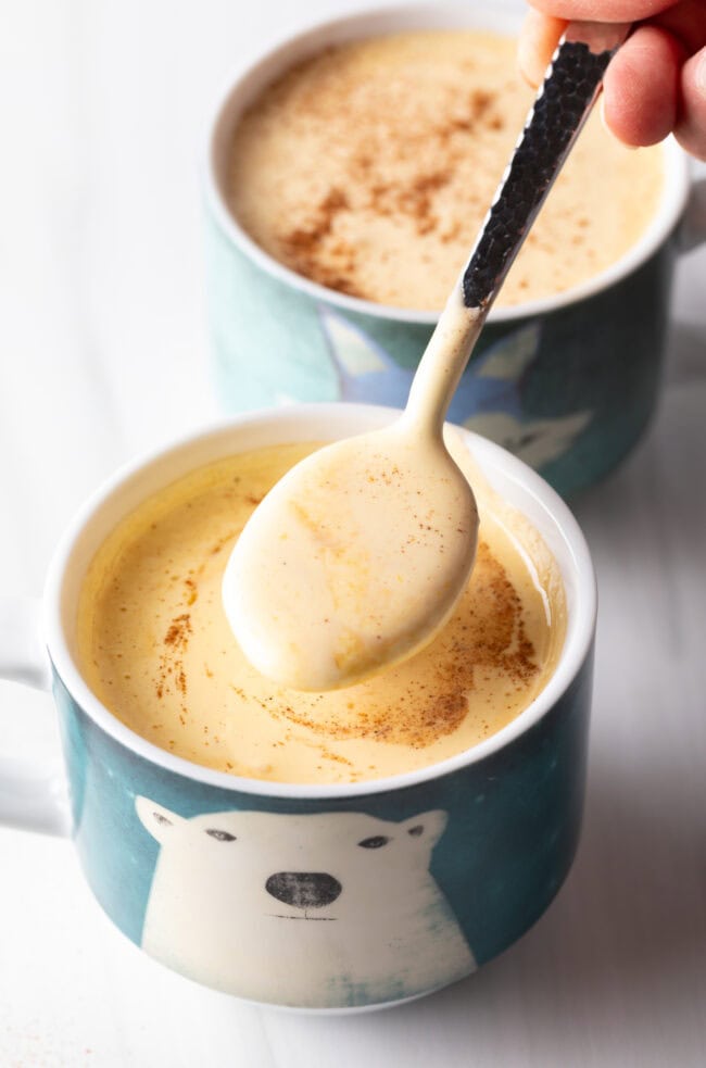 Spoon adding custard to a blue coffee mug.
