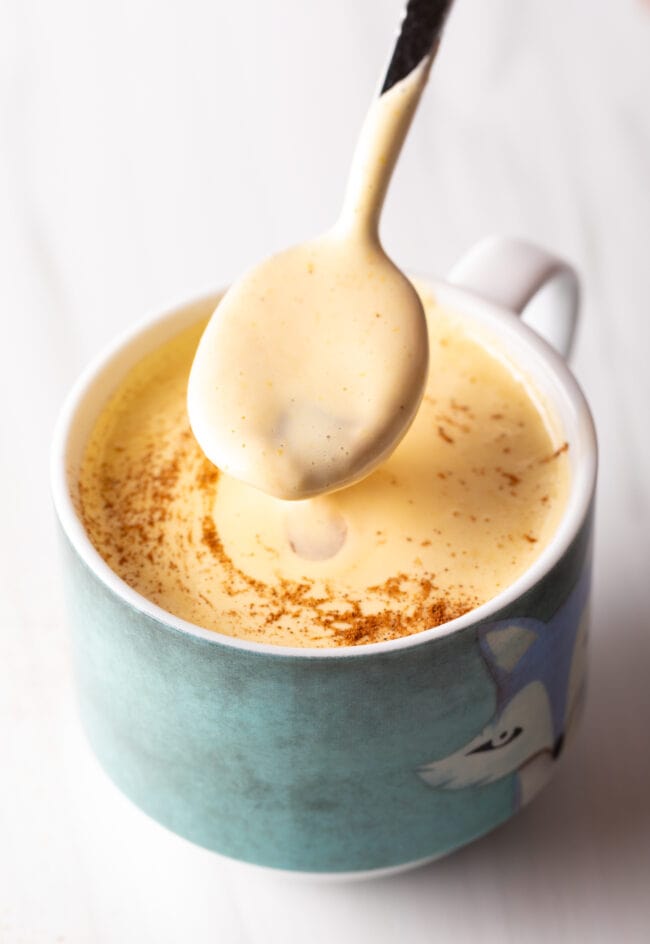 Spoon adding custard to a blue coffee mug.