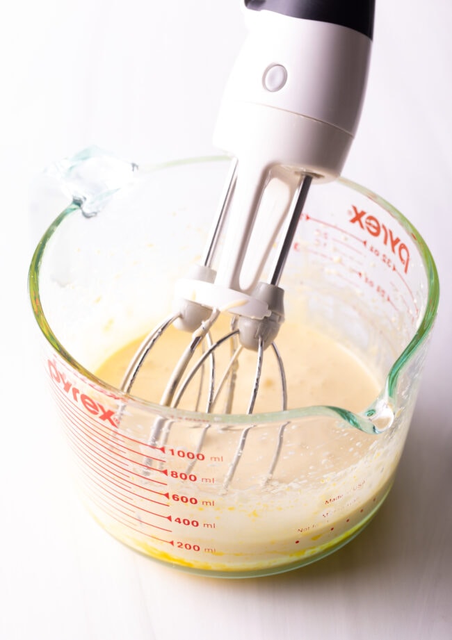 Using a handheld mixer to whip up the custard in a glass measuring bowl.
