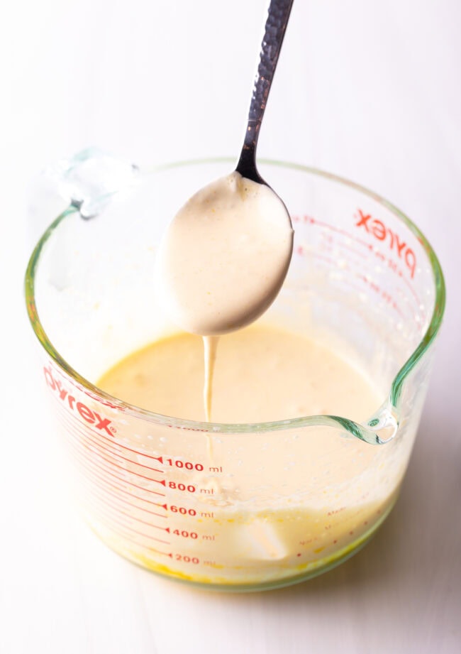 Spoon stirring custard mixture in a glass measuring bowl.