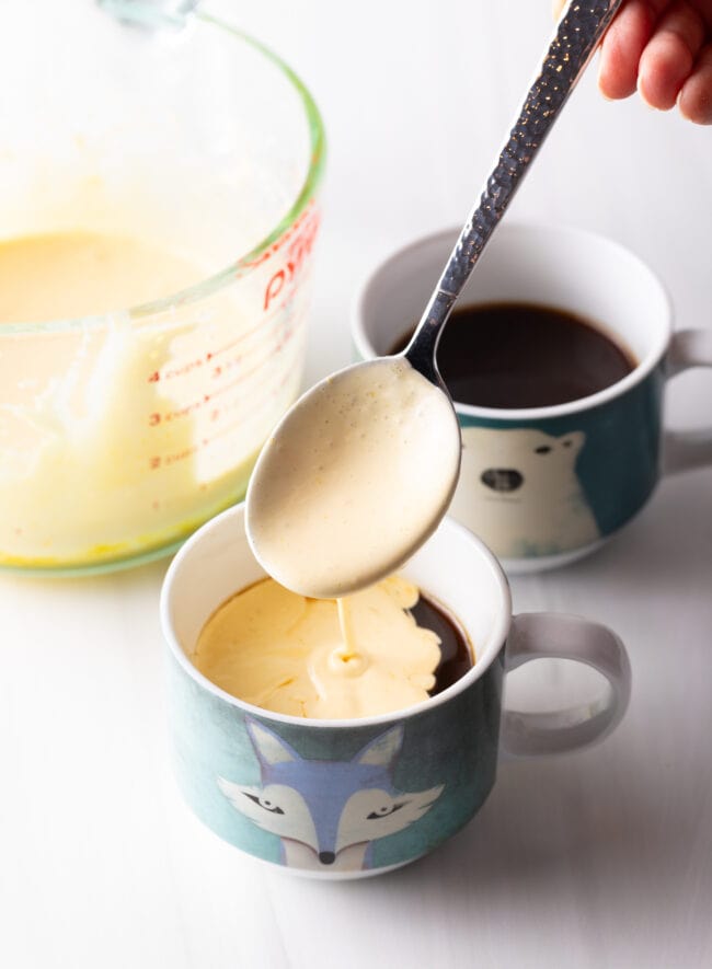 Spoon adding custard to a blue coffee mug.
